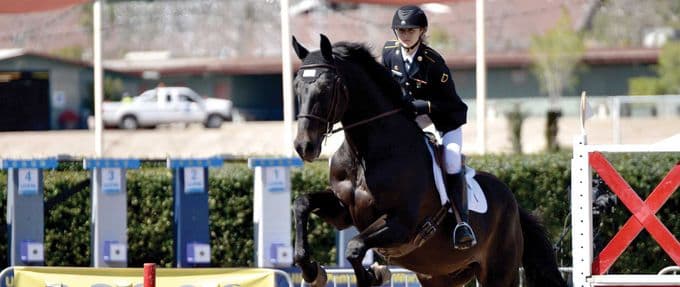 an olympic athlete and soldier jumps over an obstacle with her horse