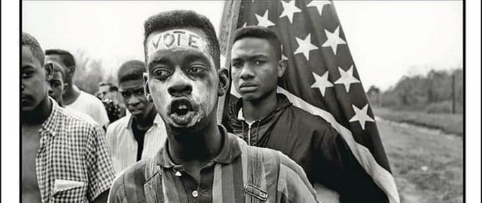 young man with the word 'vote' written on his forehead stands in front of an american flag