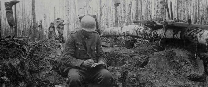 Soldier, writing a letter home amidst rubble from a battle in the woods.