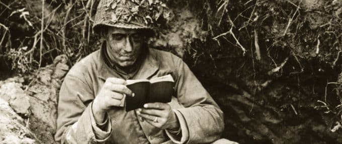 a partially camouflaged soldier reads a book